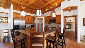 Una cocina amplia con armarios de madera, una isla grande con taburetes de bar, electrodomésticos de acero inoxidable y una chimenea de piedra.