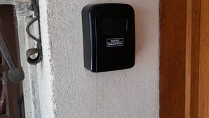A black intercom mounted on a textured wall near a wooden door.