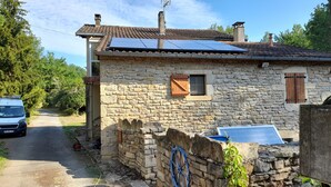 A stone house with a tiled roof, a small window with shutters, and a solar water heater.