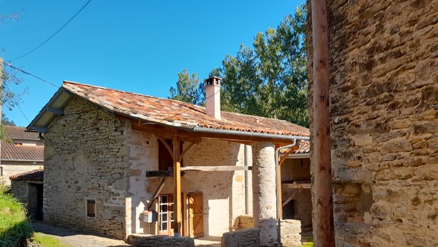 A rustic stone building with a tiled roof, a wooden porch, and a gravel driveway.