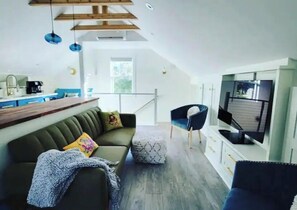 Relax in this open-plan living space with a kitchen area, featuring a sofa, ottoman, and armchair.