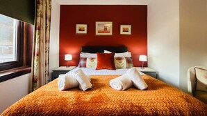 Ein Hotelzimmer mit einem Bett, zwei Nachttischen, einem fenster mit Vorhängen und drei gerahmten Bildern an der Wand.
