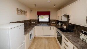 A compact kitchen with a washing machine, a sink, a stove, and a window with a red curtain.