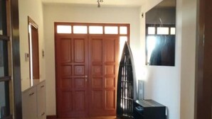 Un couloir doté d’un plancher en bois, une grande porte en bois, un portail en métal noir et une petite table avec une chaise.
