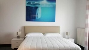 Une chambre à coucher comprenant un lit, deux tables de chevet, une petite table et un tableau représentant une cascade, accroché au mur.
