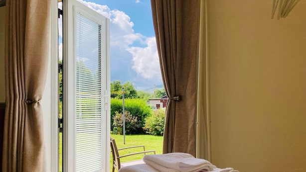A room with a view of a garden through a window with blinds. There is a stack of folded towels on the floor. - The Nell in Central Fort William (Fort William)
