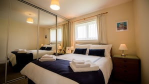 A hotel room with a large bed, a bedside table with a lamp, a mirror, and a window with curtains. - The Nell in Central Fort William (Fort William)