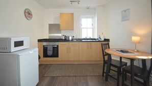 Cocina compacta con microondas, horno y lavamanos. Hay un comedor con mesa y sillas.