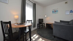 Un espacio habitable pequeño con una mesa de comedor, dos sillas, un sofá, un televisor y una lámpara.
