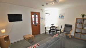 Un salon comprenant un canapé, une petite table, un fauteuil, une bibliothèque et un téléviseur à écran plat fixé au mur.
