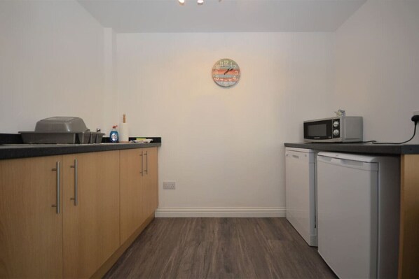 A compact kitchen with wooden cabinets, a microwave, and a dishwasher. - Puffin Apartment located on Tobermory High Street (Tobermory, Isle of Mull)