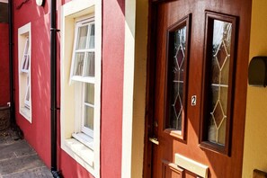 A red building with a white window and a wooden door with a number '2' on it. - Puffin Apartment located on Tobermory High Street (Tobermory, Isle of Mull)