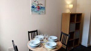 Un coin repas avec une table ronde dressée pour quatre personnes, une bibliothèque en bois et un tableau accroché au mur.