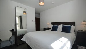Une chambre d’hôtel avec un grand lit, un bureau, une chaise, un miroir et deux lampes de chevet.