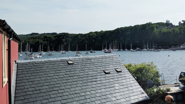 Un port avec des bateaux, un bâtiment rouge et une vue sur une colline boisée.