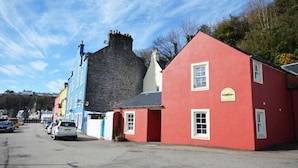 Un bâtiment rouge avec une enseigne, un mur de pierre et des voitures garées le long d’une rue.