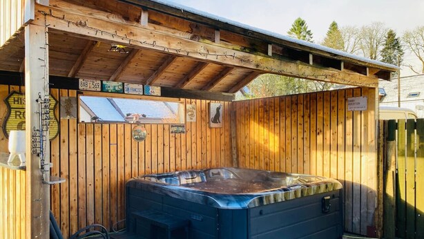 A wooden cabin with a hot tub, a chair, and a sign indicating a rental price. - Aonachan Cottage in the village of Spean Bridge (Spean Bridge)