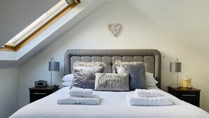 A neatly made bed with a heart-shaped wall decoration, two bedside tables with lamps, and a skylight above. - Aonachan Cottage in the village of Spean Bridge (Spean Bridge)