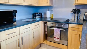 A kitchen with wooden cabinets, a microwave, a toaster, and an oven. - Aonachan Cottage in the village of Spean Bridge (Spean Bridge)