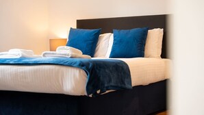 A neatly made bed with blue and white bedding, a dark headboard, and a lamp on the nightstand. - Achintee Cottages No 1 (Highland Council)