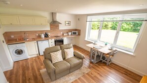 A compact kitchen with a washing machine, a dining area with a table and chairs, and a sofa with cushions. - Achintee Cottages No 1 (Highland Council)