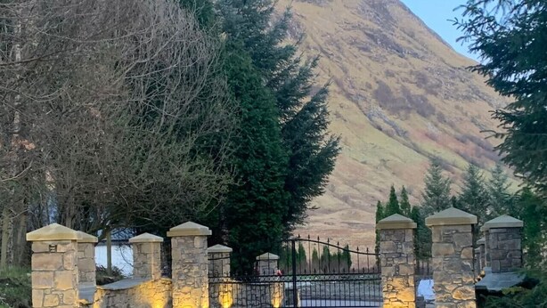 A gated entrance with stone pillars and a metal gate, leading to a mountainous landscape. - Achintee Cottages No 1 (Highland Council)