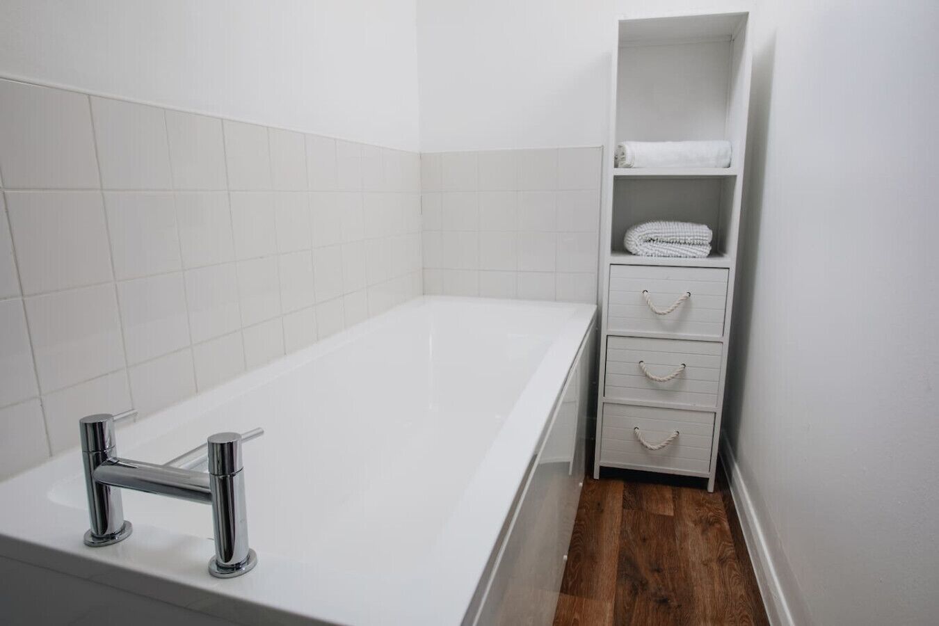 A bathroom with a white bathtub, chrome faucet, and a wooden floor.
