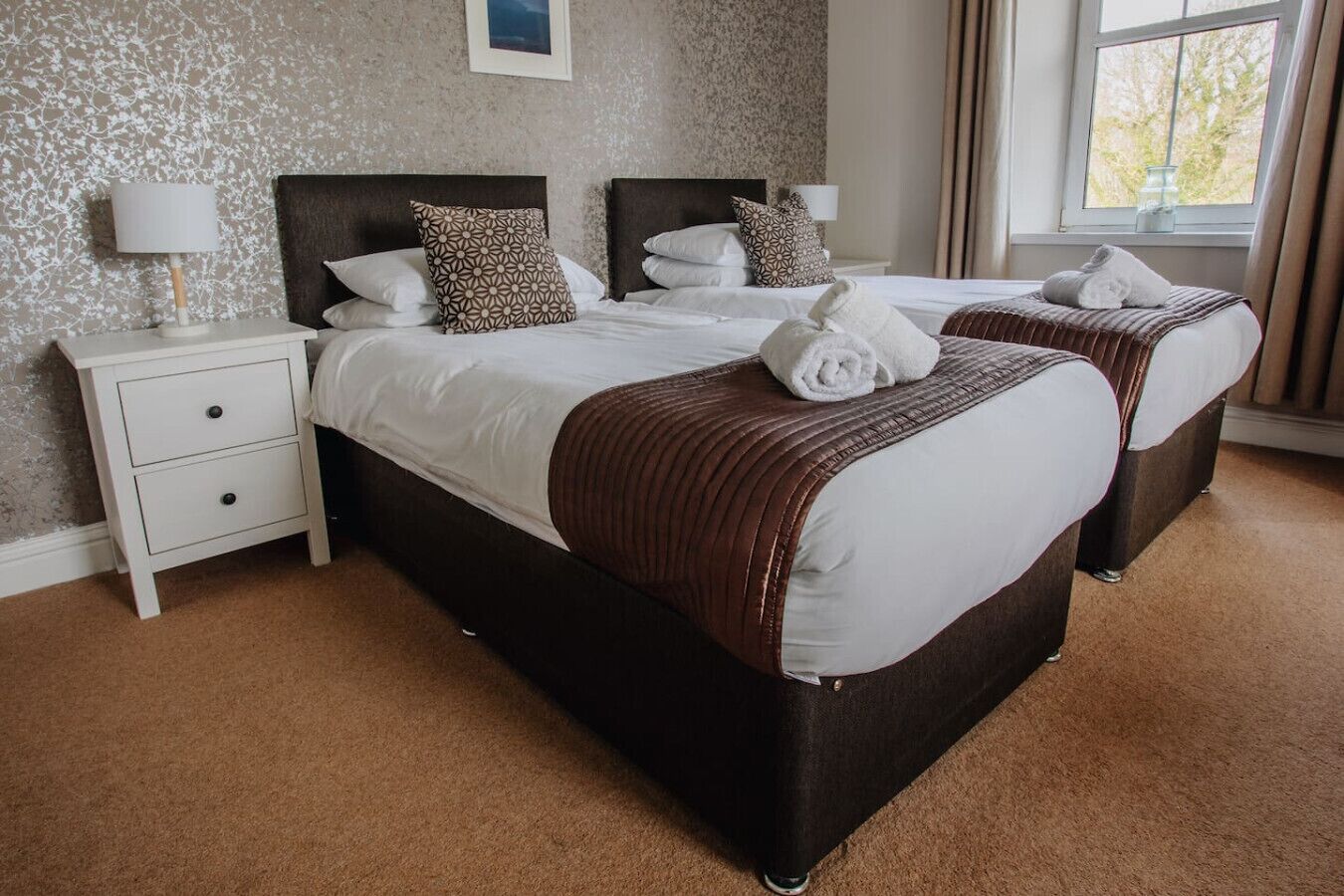 A hotel room with two beds, a nightstand, and a window with curtains.