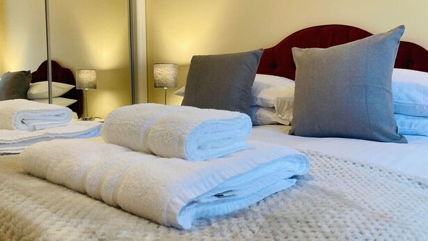 A neatly made bed with white and blue towels, a red headboard, and a bedside lamp.