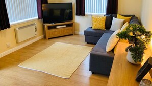 A living room with a sofa, a television, a small table, and a potted plant.
