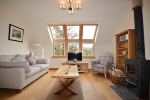 A cozy living room with a sofa, a coffee table, a television, a fireplace, and a bookshelf.