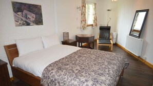 Un dormitorio con una cama grande, una silla, una mesita, un radiador y un cuadro en la pared.