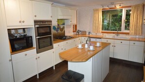 Una cocina con armarios blancos, encimera de madera, un fregadero y una ventana con cortinas.