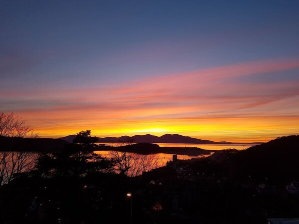 A sunset over a body of water with distant hills.