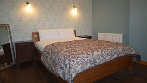 Un dormitorio con una cama de madera, dos mesitas de noche, una mesita auxiliar, un espejo y dos luces fijadas a la pared.