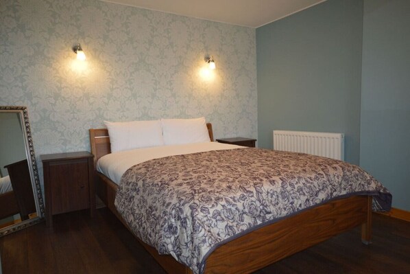 A bedroom with a wooden bed, two bedside tables, a nightstand, a mirror, and two wall-mounted lights. - Ardura Apartment No 2 (Oban)