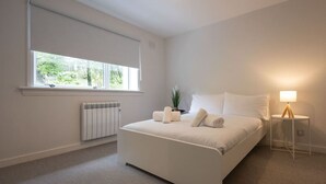 A modern bedroom with a large bed, a radiator, a window with a view, and a bedside lamp. - Highland Lookout in Fort William (Highland Council)