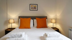 A neatly made bed with white linens and two orange pillows, flanked by two bedside lamps on matching nightstands. - George Street Apartment (Oban)