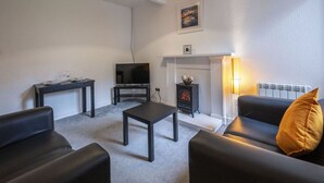 A living room with a fireplace, a TV, and a sofa. - George Street Apartment (Oban)