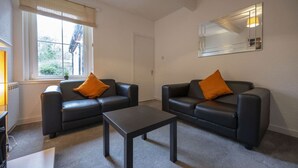 A modern living room with two black leather sofas, each with an orange cushion, a small black coffee table, and a large mirror on the wall. - George Street Apartment (Oban)
