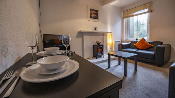 A dining area with a fireplace, a sofa, and a table set for two. - George Street Apartment (Oban)