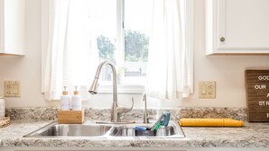 A kitchen with white cabinets, a stainless steel sink, and a window with sheer curtains.