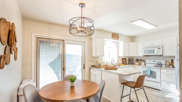 A modern kitchen with white cabinets, a wooden dining table, and a hanging light fixture.