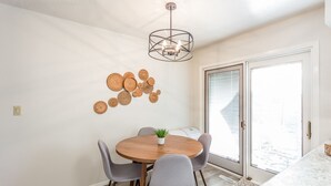 A dining area with a round wooden table, grey upholstered chairs, a hanging light fixture, and a wall-mounted decorative arrangement.