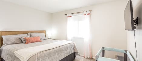 Un dormitorio con cama, televisor montado en la pared y ventana con cortinas.