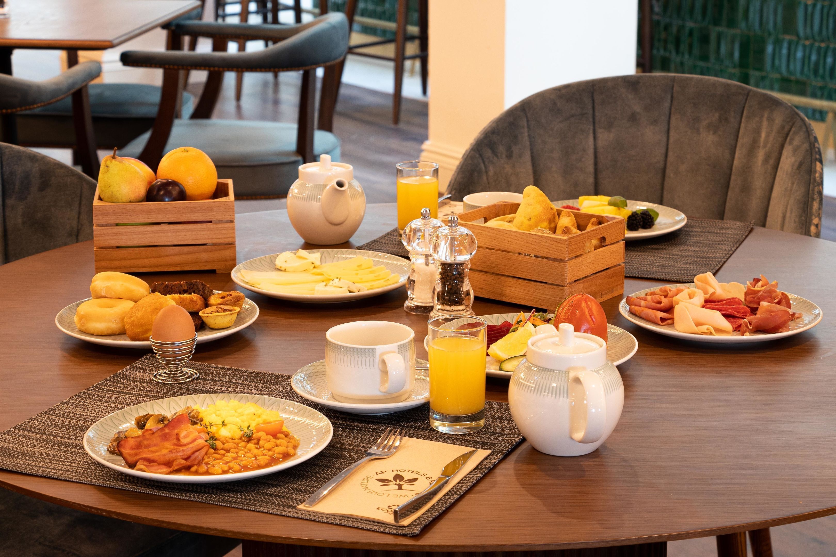 Una escena de desayuno con diversos platos, una tetera y una jarra de jugo de naranja sobre una mesa de madera.