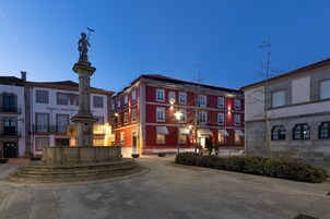 Una plaza con una fuente central y edificios circundantes, incluyendo un edificio rojo con un letrero que dice "ESCOLA MASTRO JORRO".
