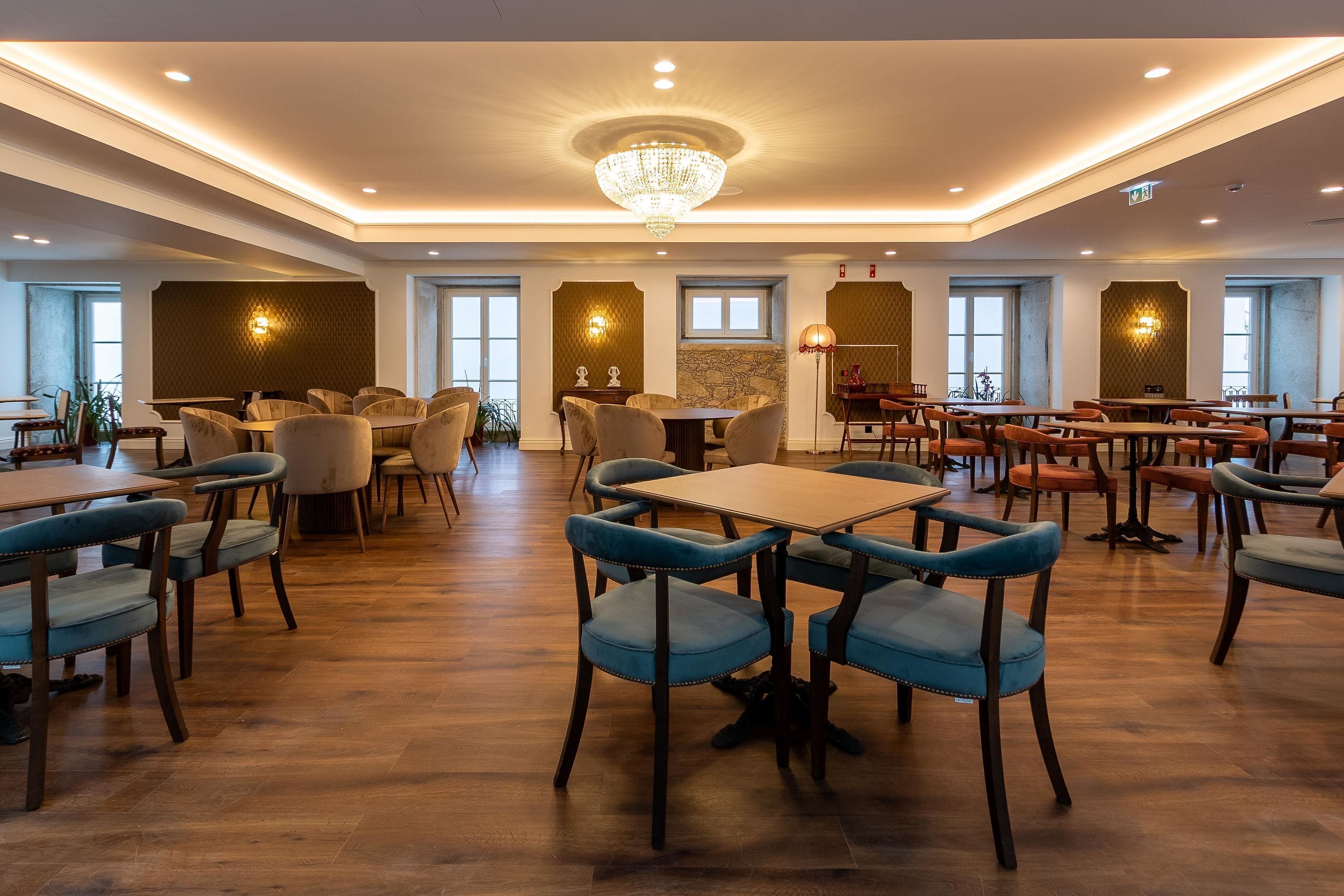 A spacious dining area with multiple tables and chairs, a chandelier, and decorative wall sconces.