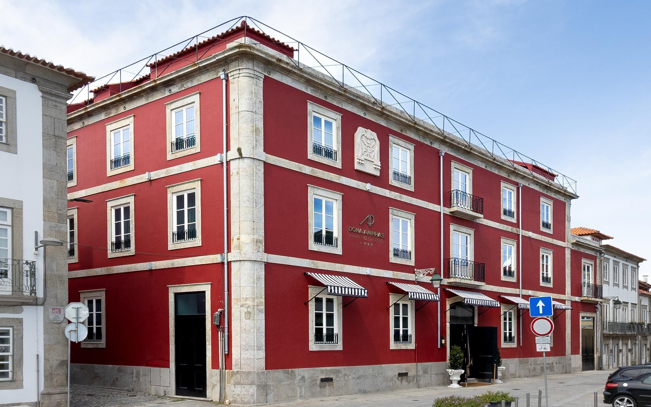 A red building with multiple windows, a sign reading "Dona Aninhas," and a blue directional sign.