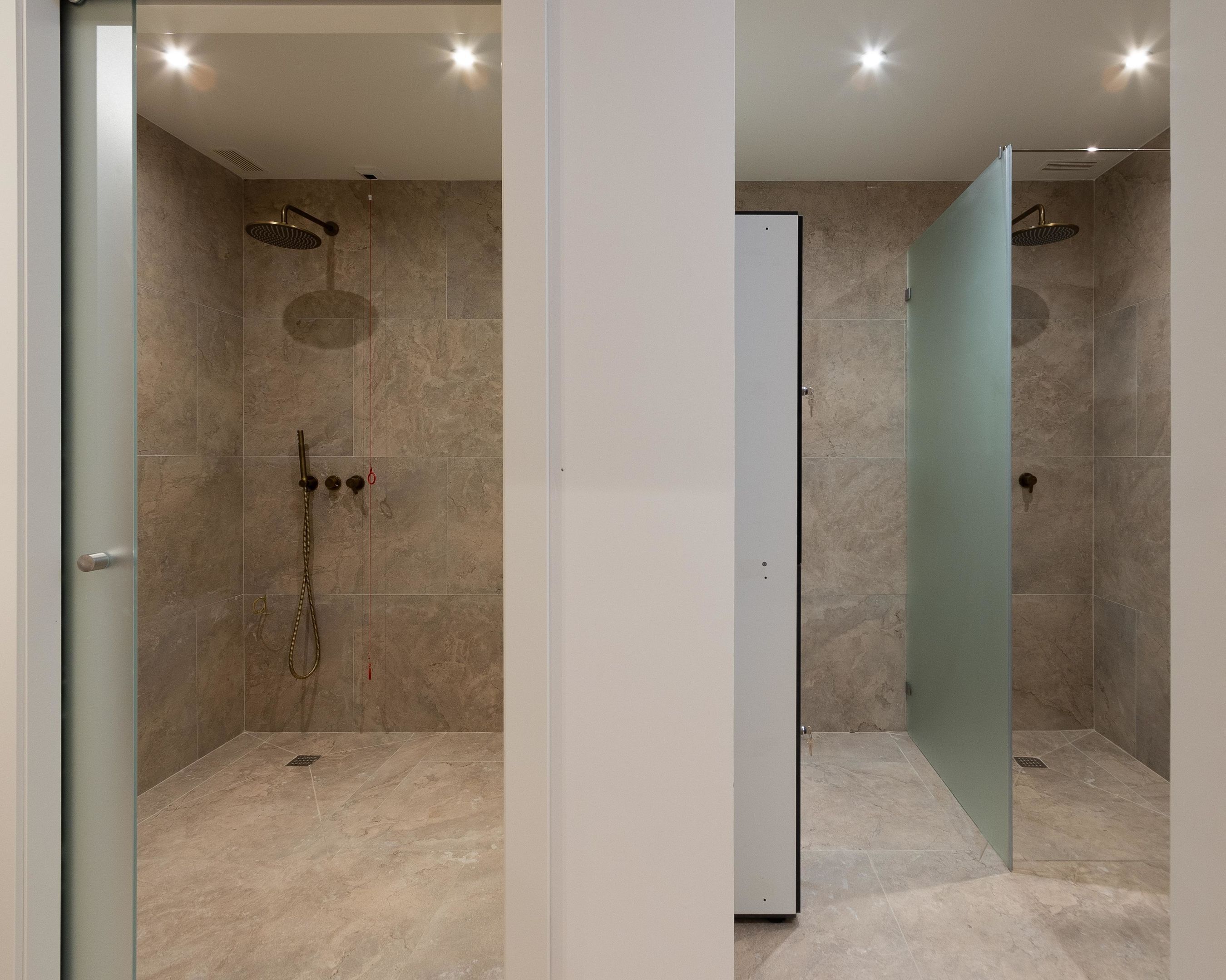 A modern bathroom with a glass shower enclosure, a white door, and a tiled floor.